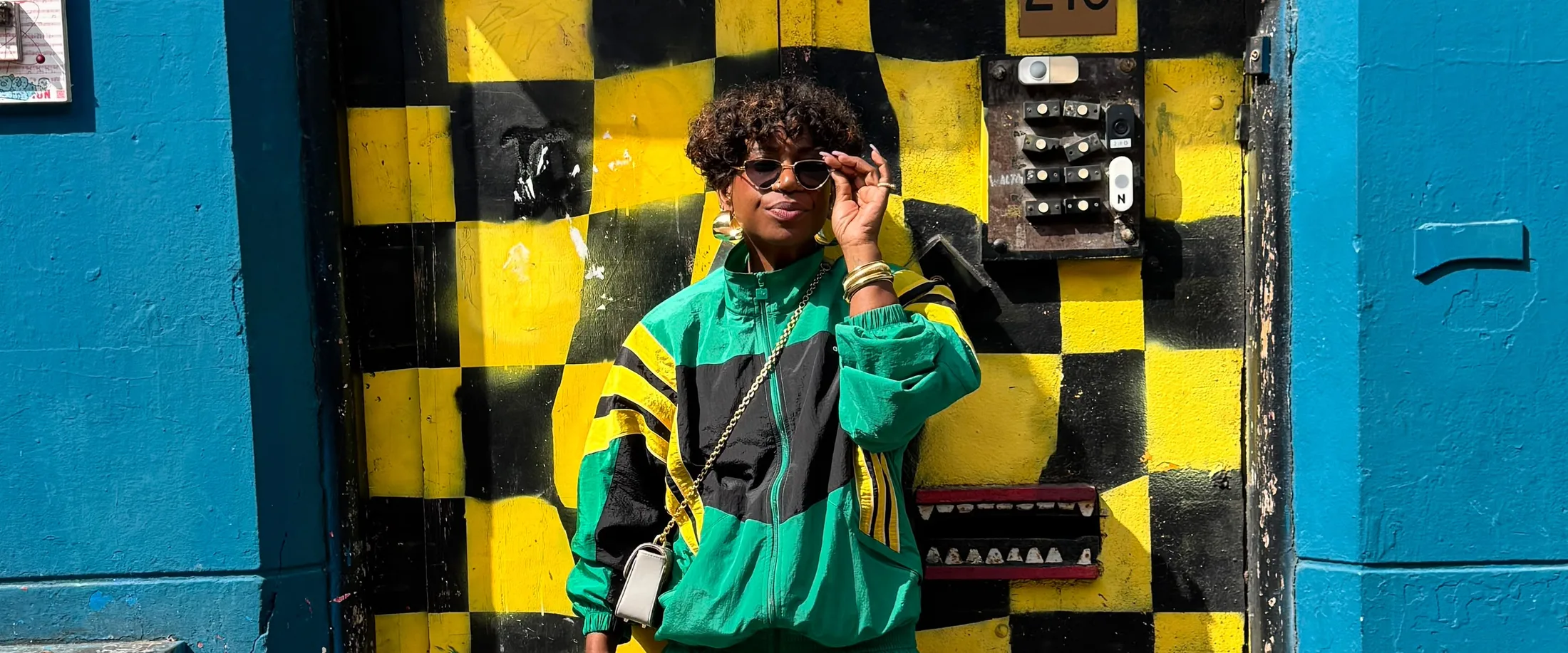 Dayenne Bekker in a green and yellow track jacket in front of a yellow and black checkerboard door